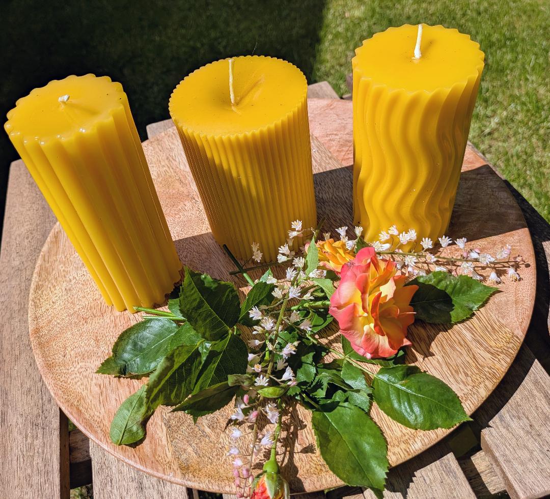 Drei große Bienenwachsstumpen mit unterschiedlichen Linienmustern auf Holzscheibe mit Rose