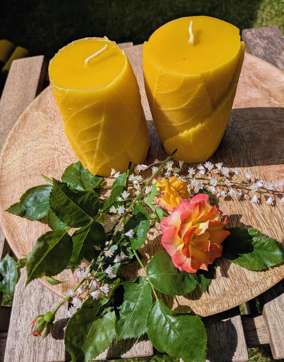 Zwei Bienenwachsstumpen mit eingedrücktem Blattrelief auf Holzscheibe mit Rosen