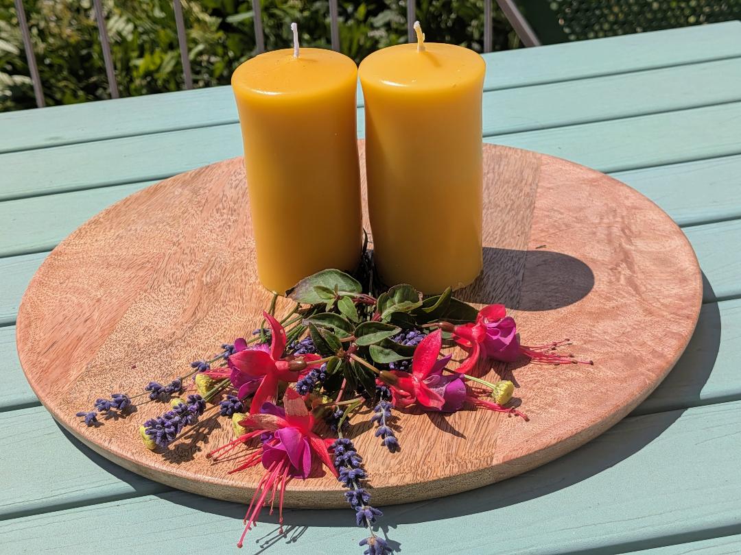 Zwei mittlere Bienenwachsstumpen auf Holzscheibe mit pinkfarbenen Fuchsien