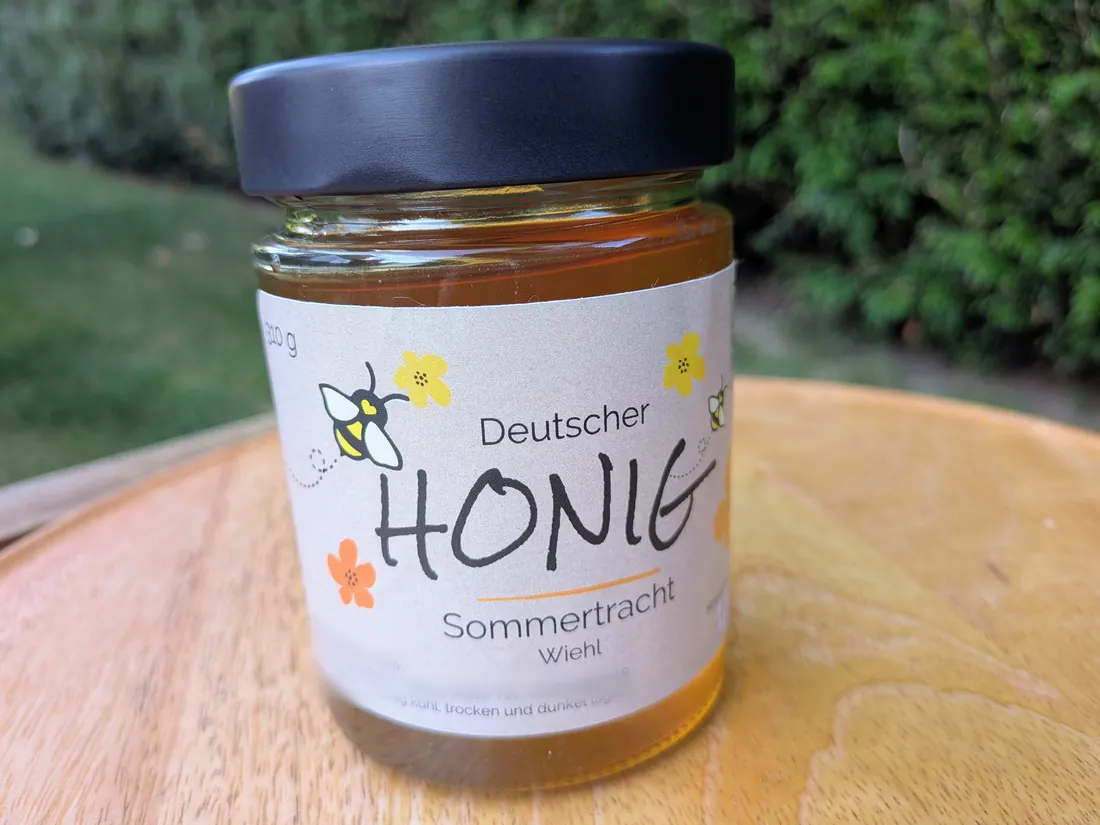 Ein 310-g-Glas Sommertrachthonig aus der Nähe, das Etikett mit gezeichneten Bienen und Blüten gut lesbar