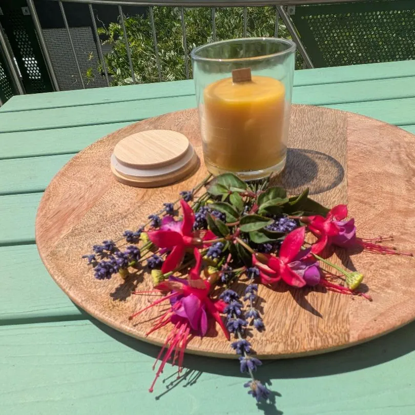 Bienenwachskerze im Glas mit Holzdocht auf Holzscheibe mit Fuchsien, Holzdeckel daneben