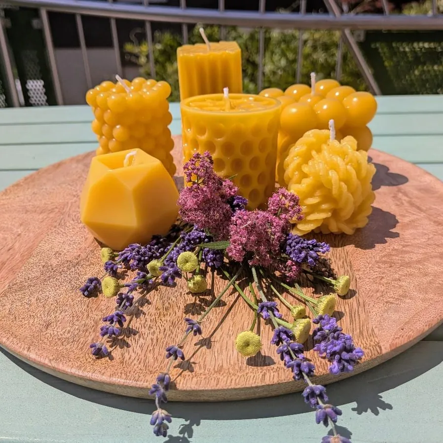 Sechs verschiedene kleine Bienenwachskerzen in unterschiedlichen Formen auf Holzscheibe mit Blumen