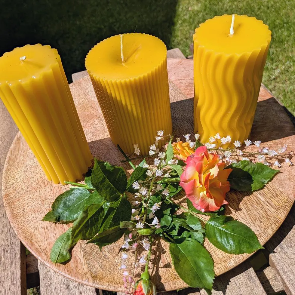 Drei große Bienenwachsstumpen mit breiten, feinen und gewellten Rillen auf Holzscheibe mit Rose
