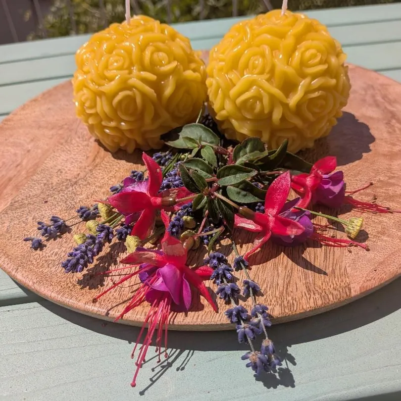Zwei kugelförmige Bienenwachskerzen mit Rosenrelief auf Holzscheibe, mit Fuchsien und Lavendel