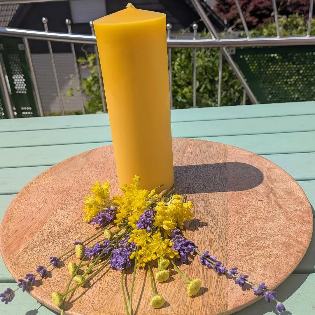 Großer schlanker Bienenwachsstumpen auf Holzscheibe, umgeben von Lavendel und Wiesenblumen