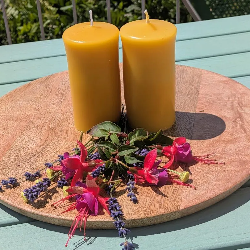 Zwei mittlere Bienenwachsstumpen auf Holzscheibe mit pinkfarbenen Fuchsien
