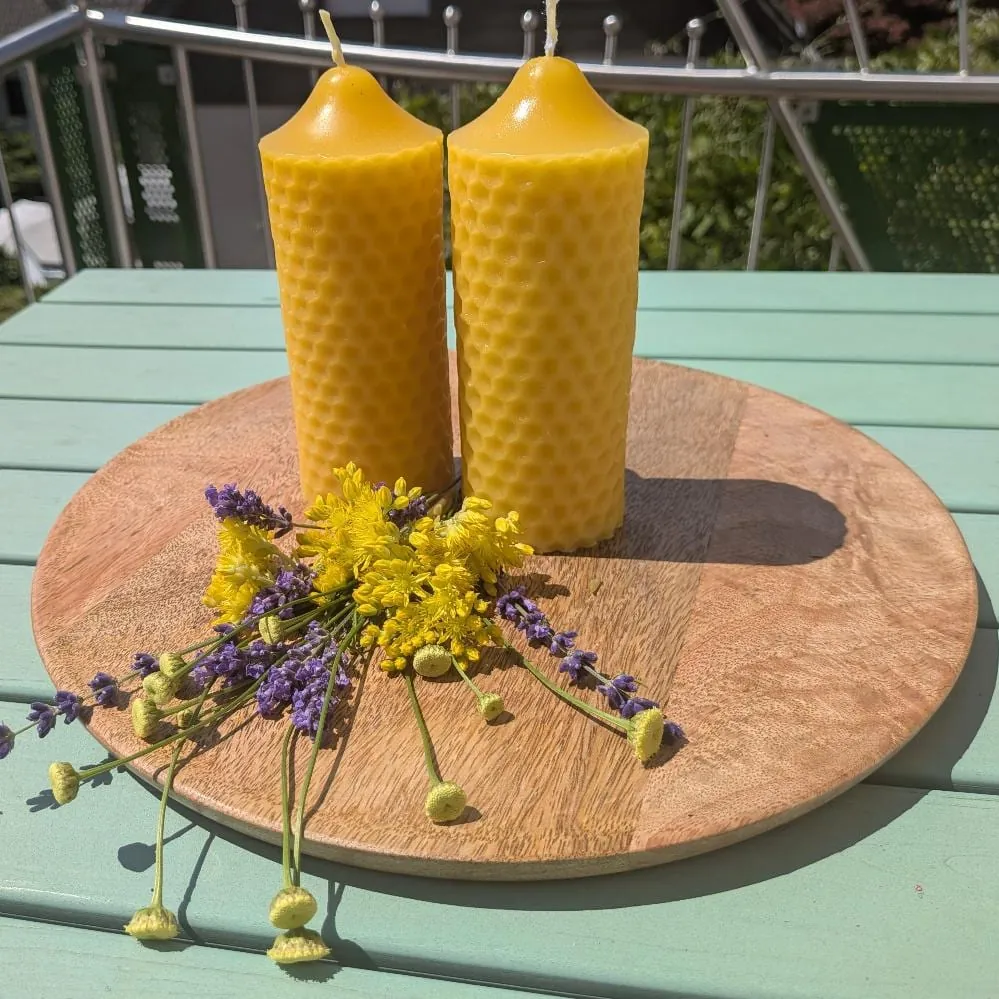 Zwei schlanke Bienenwachskerzen mit Wabenrelief auf Holzscheibe, mit Lavendel und Wiesenblumen
