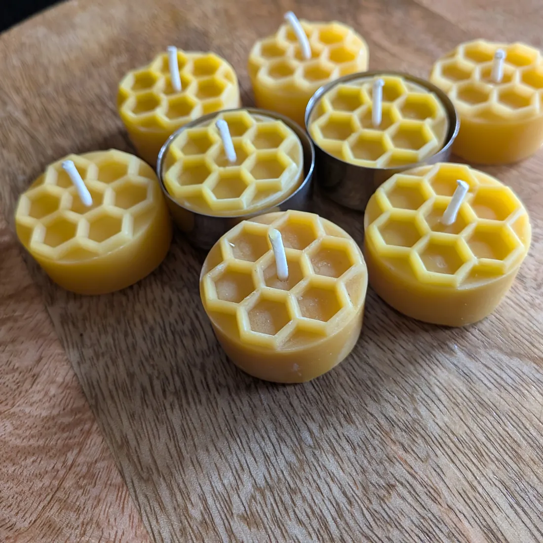 Acht Bienenwachsteelichter mit Wabenmuster, zwei davon in Edelstahlhüllen, auf Holzscheibe