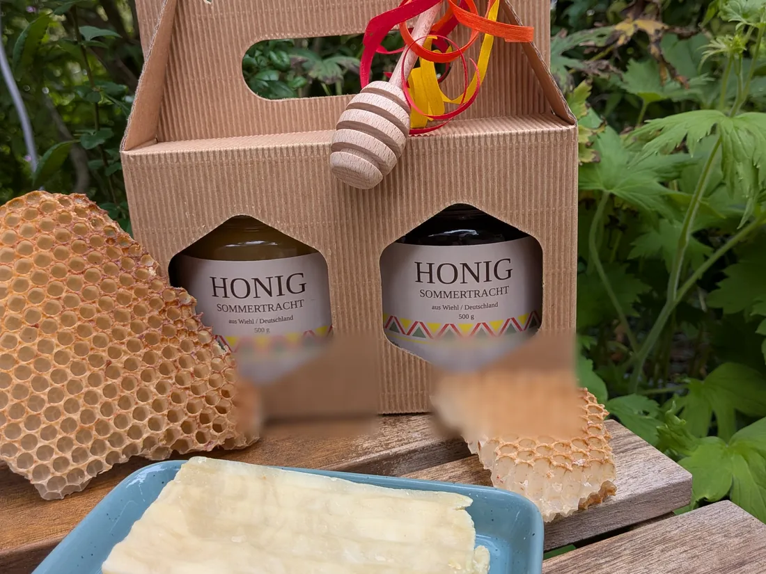 Geschenkkarton mit zwei Gläsern Honig, Wabenstücken und der cremefarbenen Arganöl-Olivenölseife auf einer blauen Schale