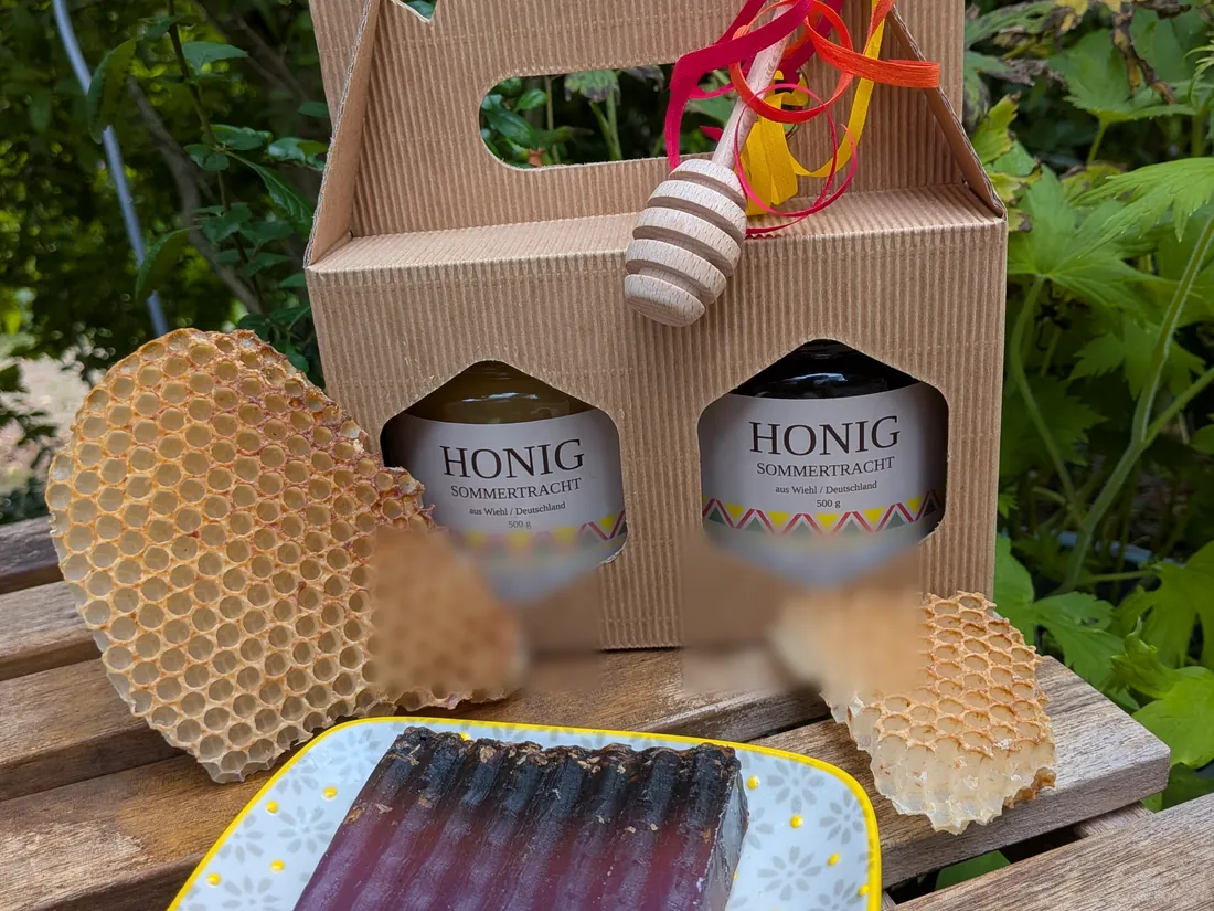 Geschenkkarton mit zwei Gläsern Honig, Wabenstücken und der dunklen, geriffelten Lavendelseife auf einer gelb umrandeten Schale