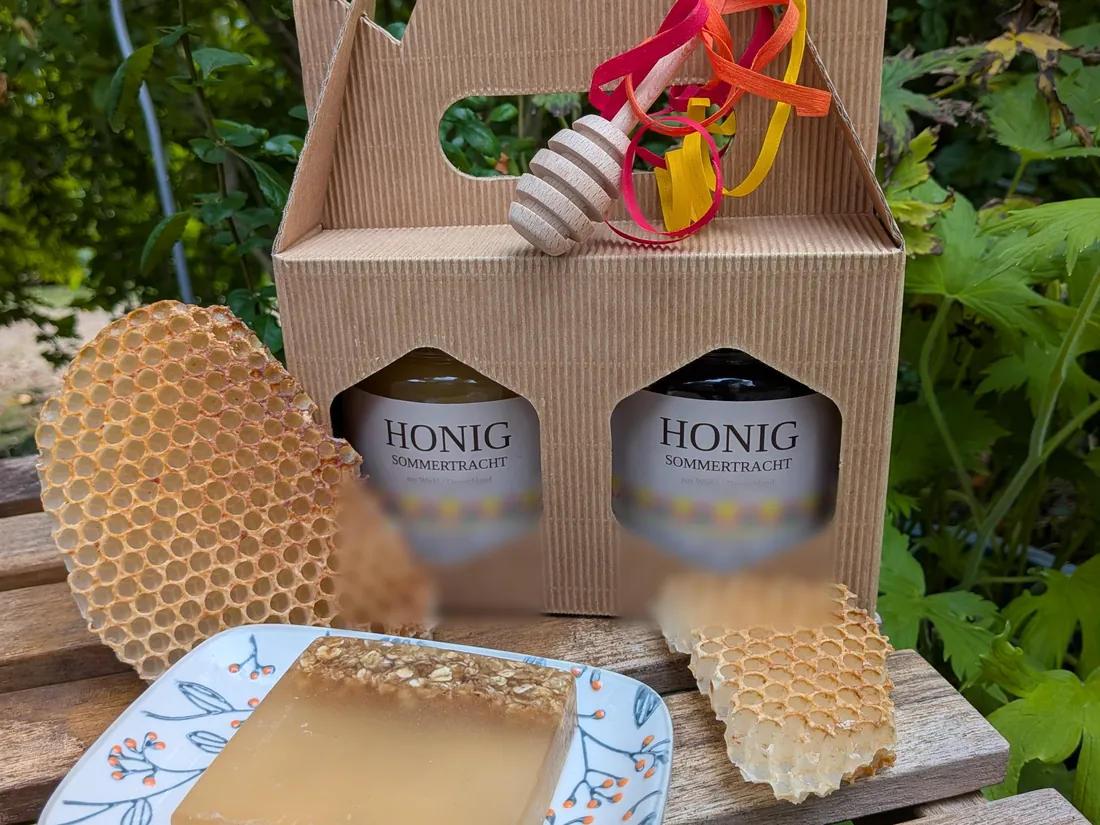 Geschenkkarton mit zwei Gläsern Honig, Wabenstücken und der Honig- und Haferflockenseife auf einer weißen Schale