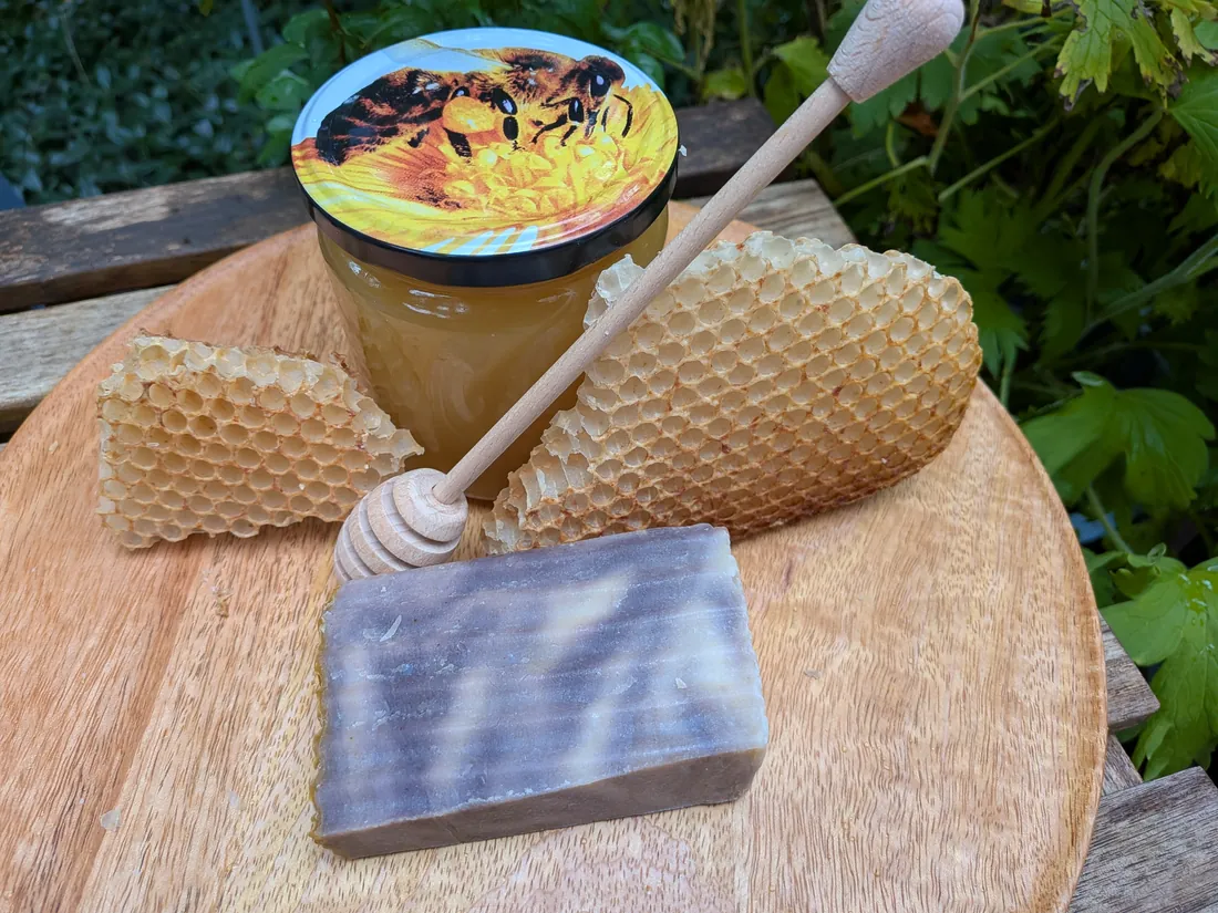 Bienenharz-Olivenölseife, grau-braun marmoriert, auf einem Holzbrett neben Wabenstücken und einem Glas Honig