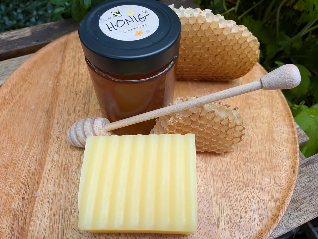 Gelbe Mandarinen-Honigseife auf einem Holzbrett, dahinter ein Glas Honig und zwei Wabenstücke