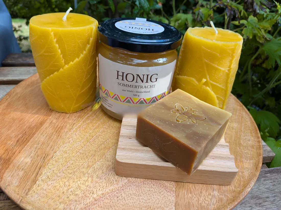 Honigseife mit Bienenprägung auf einer Holzschale, ein Glas Sommertrachthonig und zwei Bienenwachskerzen mit Blattrelief