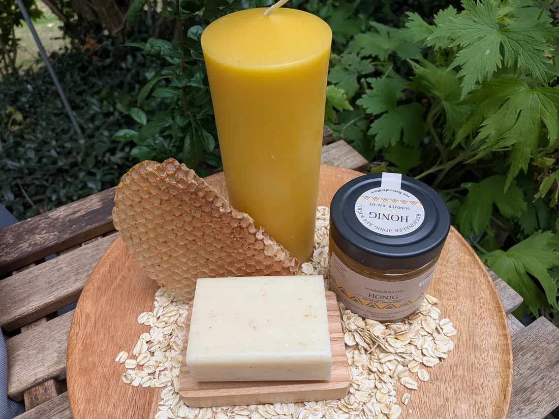 Große Bienenwachs-Stumpenkerze, Wabenstück, Honigglas und Honig-Haferflockenseife auf Holzschale zwischen Haferflocken